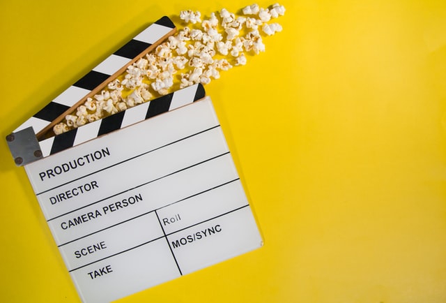 Clapboard in open position with popcorn holding it open as it lays on a yellow background